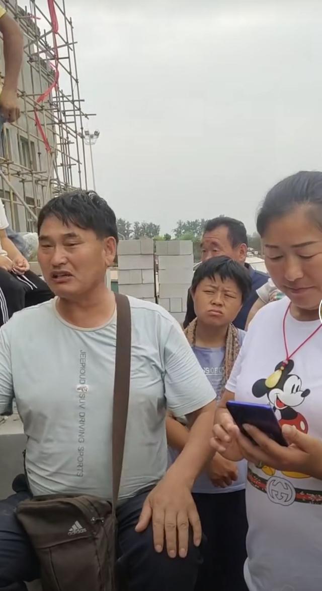 大衣哥耐心教村民唱歌，身后未建成小楼抢镜，唱歌干活两不误