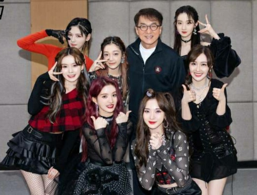 成龙与女团合影略显亲密，搭肩搂腰被批行为不当，表情像复制粘贴